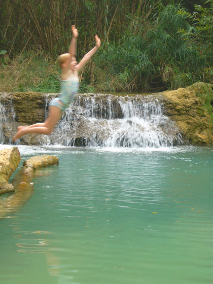 Ella jumps from the lime encrusted fallen tree into one of the many swimming holes downstream from the Kuang Si waterfall.